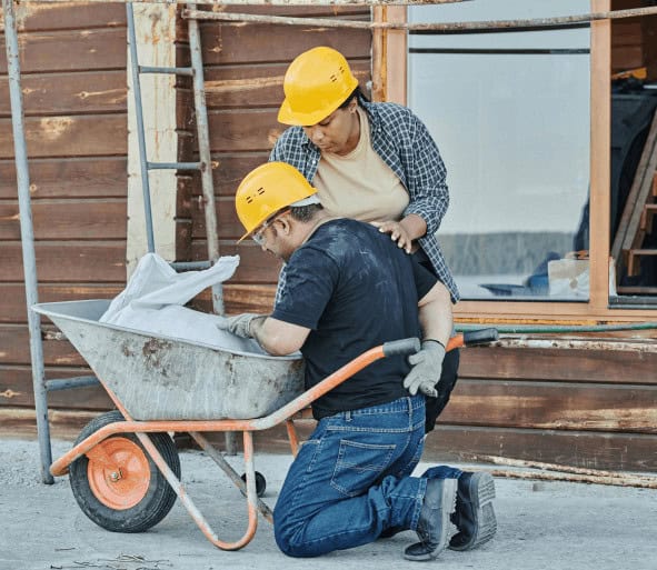 Construction worker experiencing back pain, leaning on wheelbarrow. 