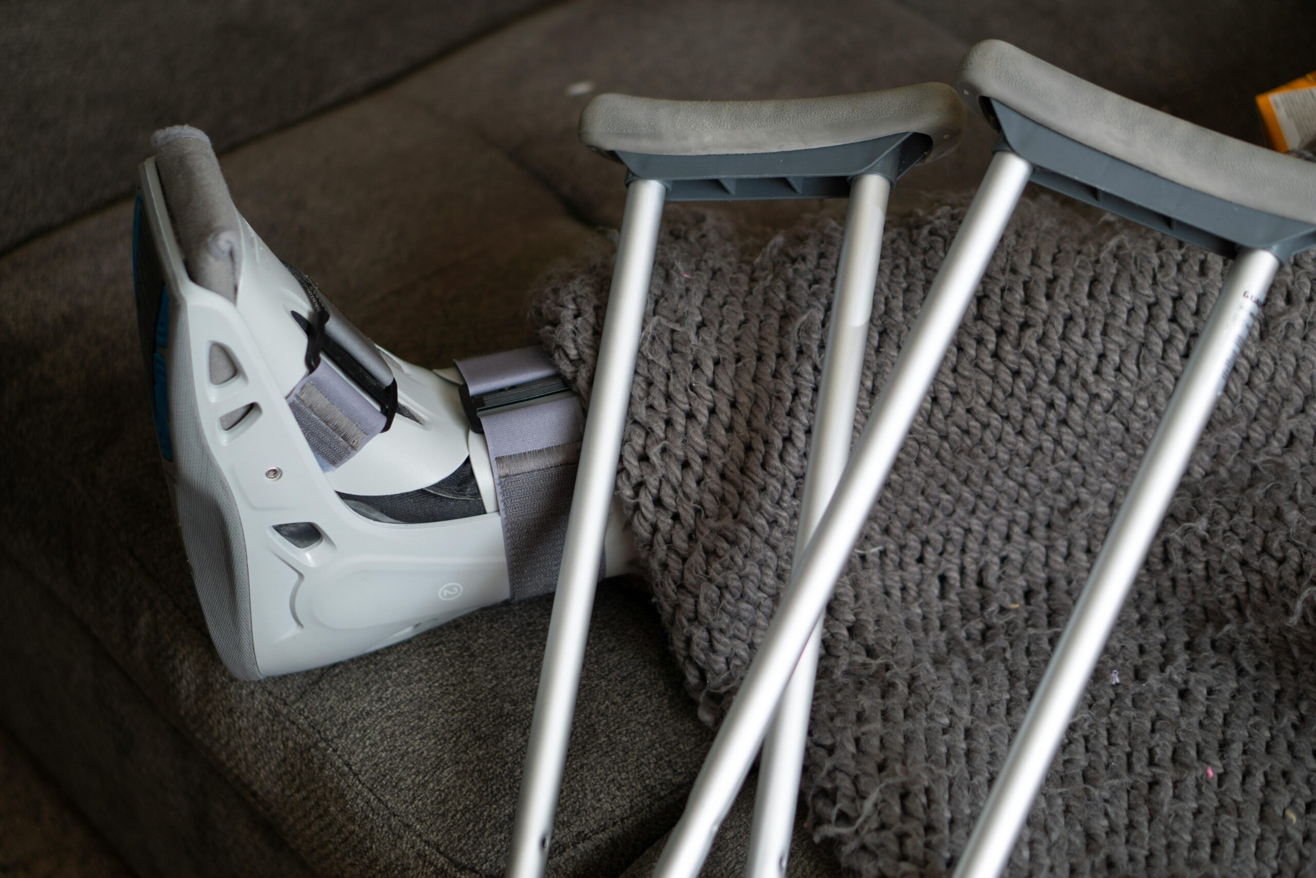 Leg in boot with crutches and blanket on a couch.