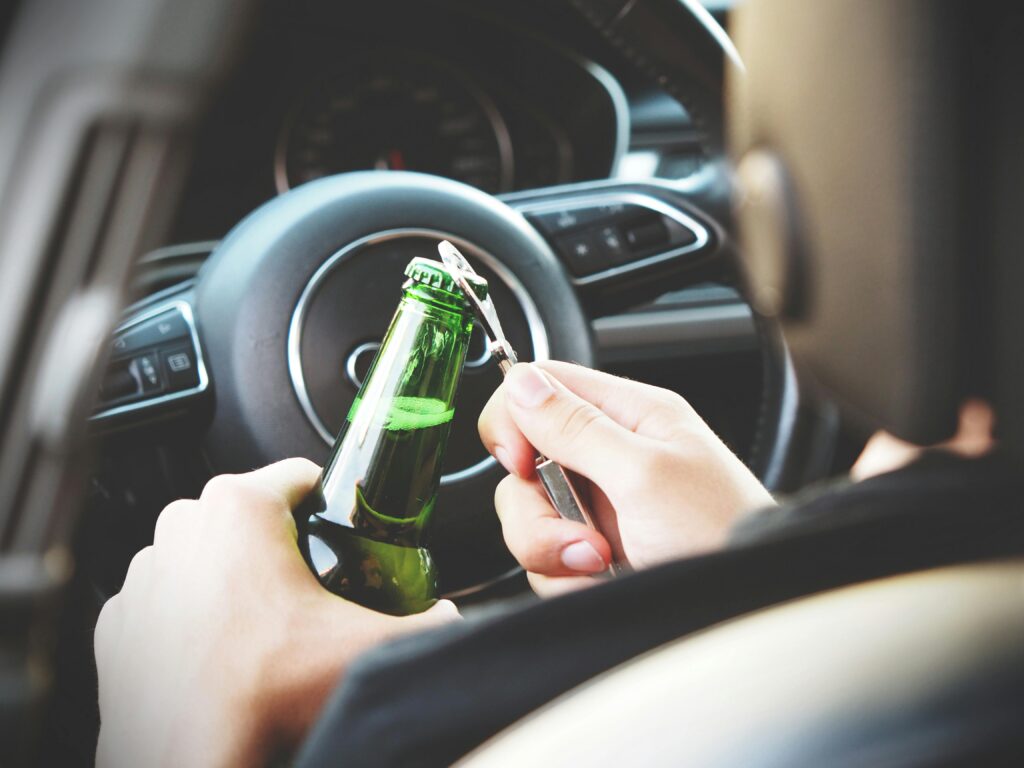 A driver opening a bottle behind the wheel potentially leading to impaired driving and car accidents.