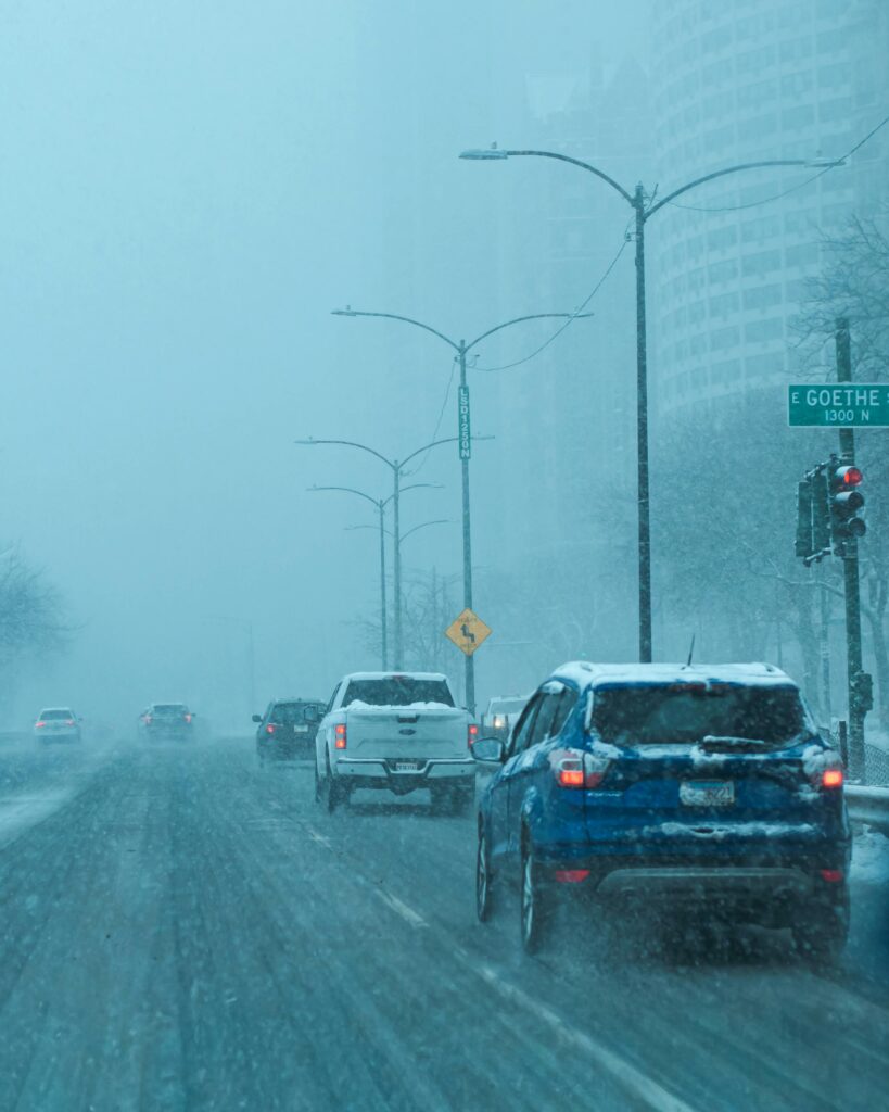 Multiple cars driving on icy/snowy roads during a storm. 